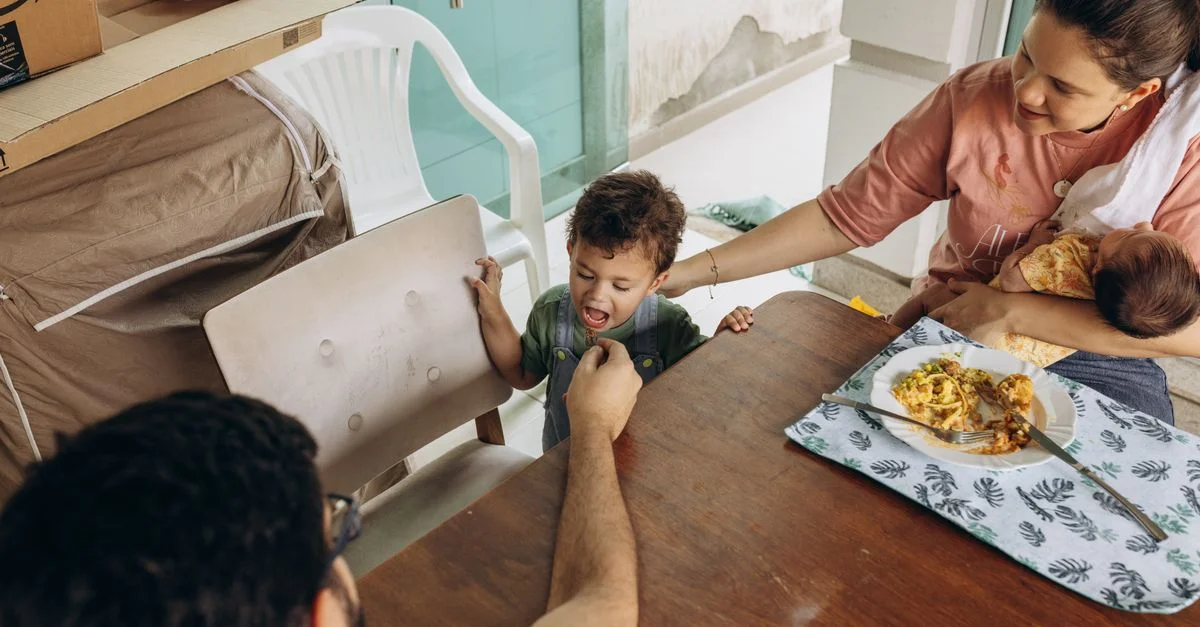 Mãe segurando o bebê enquanto cuida do filho maior na hora da refeição