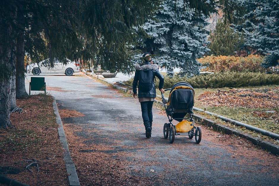 Mulher caminhando em parque urbano com carrinho de bebê, refletindo momentos de maternidade e lazer ao ar livre.