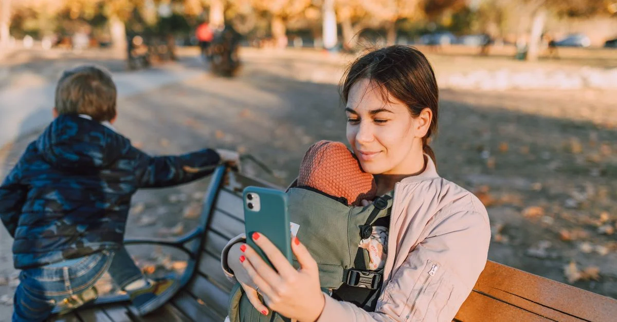 Mãe olhando o celular enquanto segura o bebê no colo