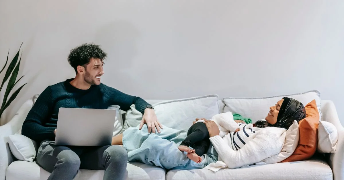 Casal conversando com carinho no sofá enquanto o bebê está por perto