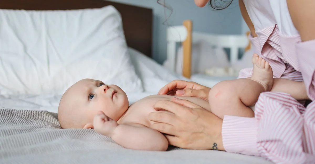 Bebê deitado na cama com a mão da mãe acariciando sua barriga